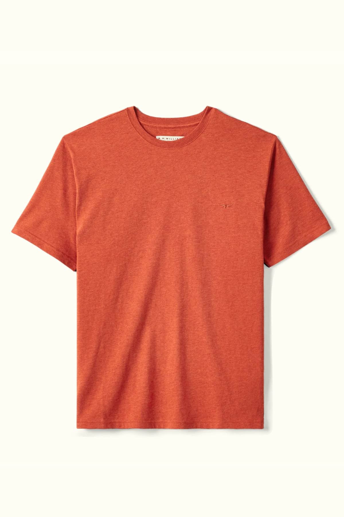 The RM Williams Parson T-Shirt is a plain, short-sleeve crew neck shirt in terracotta, crafted from soft organic cotton and featuring a subtle embroidered logo on the left chest against a light background.
