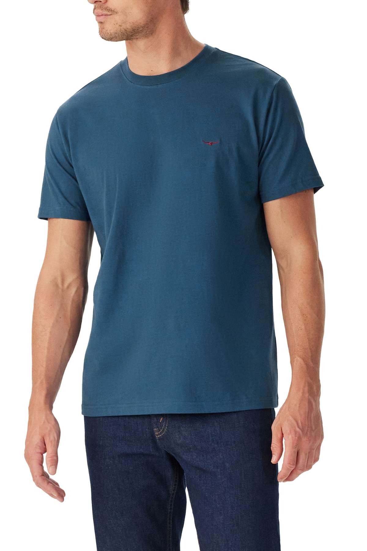 A man wearing the RM Williams Parson T-Shirt in plain teal with dark blue jeans stands slightly turned against a white background.