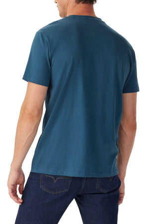 A man is seen from behind wearing a short-sleeved, teal RM Williams Parson T-Shirt and dark blue jeans against a white background.