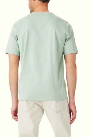 A person is wearing a light green RM Williams Parson T-Shirt made of organic cotton, featuring a classic crew neck, paired with cream-colored pants, standing with their back to the camera against a plain background.