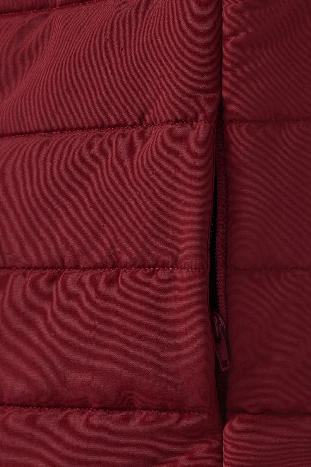 Close-up of the quilted maroon fabric, likely from the RM Williams Patterson Creek Vest. The image shows horizontal stitching and a partially visible side zipper pocket, suggesting it's a stylish yet functional water-resistant puffer vest.