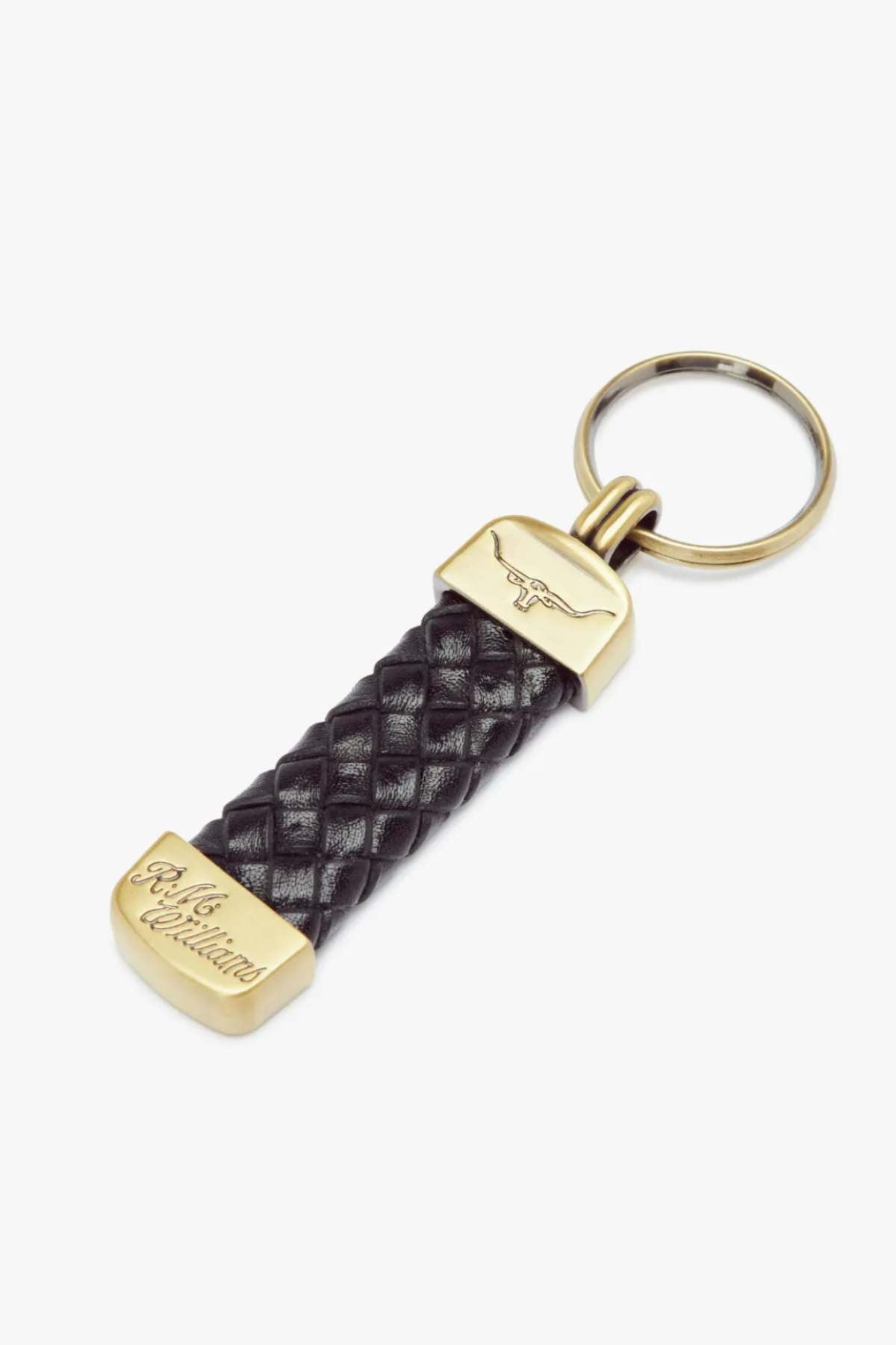 The RM Williams Plaited Key Ring includes a gold-colored metal ring and tips, a braided black kangaroo leather strap, and brass-toned fittings with engravings featuring a longhorn embossed logo and stylized text.