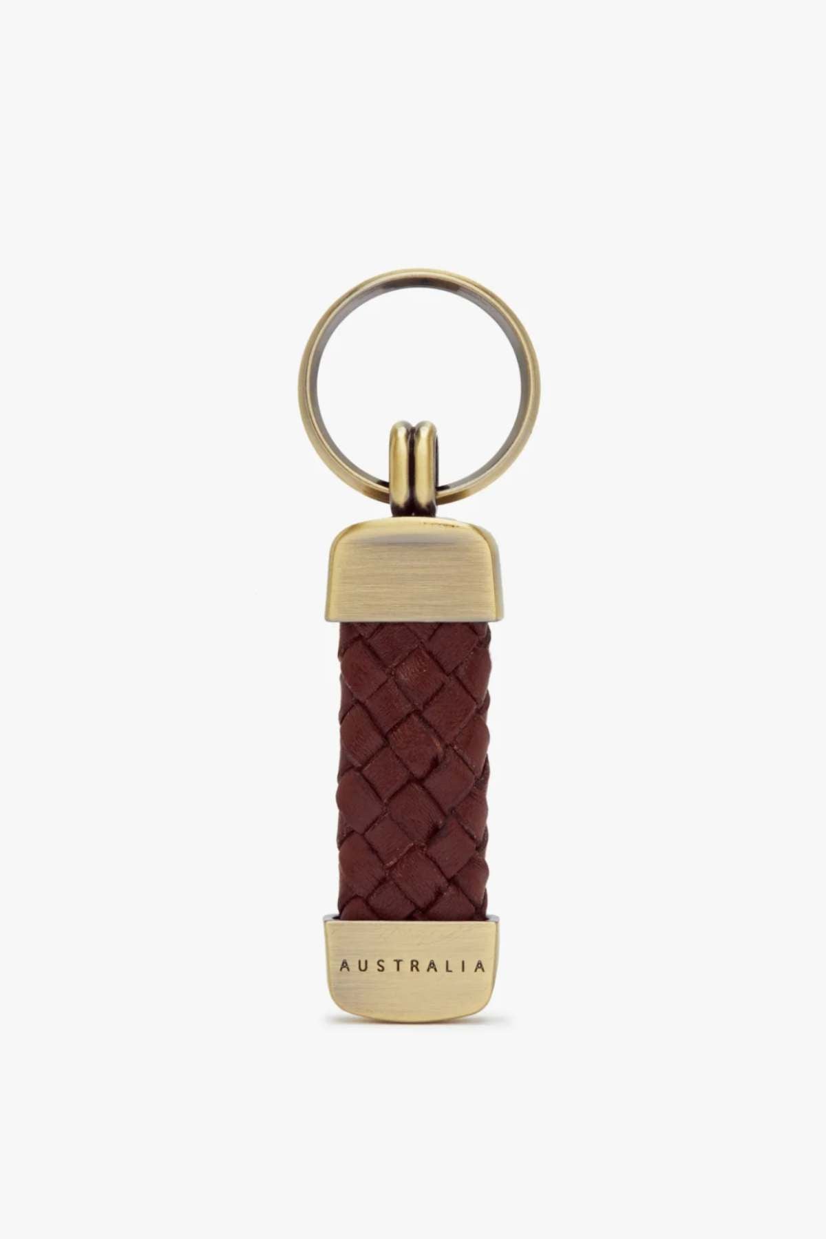 The RM Williams Plaited Key Ring features a brass keyring with a brown braided kangaroo leather body, metallic end caps, and "AUSTRALIA" engraved on the bottom, combining minimalist design with premium brass-toned fittings.