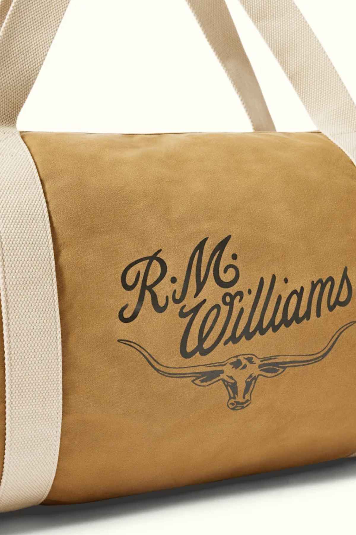 The RM Williams RM Ditty Bag is displayed, a tan duffel with white straps that makes an ideal travel companion. It showcases the R.M. Williams logo in black on the side, featuring a cattle head with horns. Crafted from leather or leather-like material, it includes an adjustable crossbody strap for added convenience while traveling.