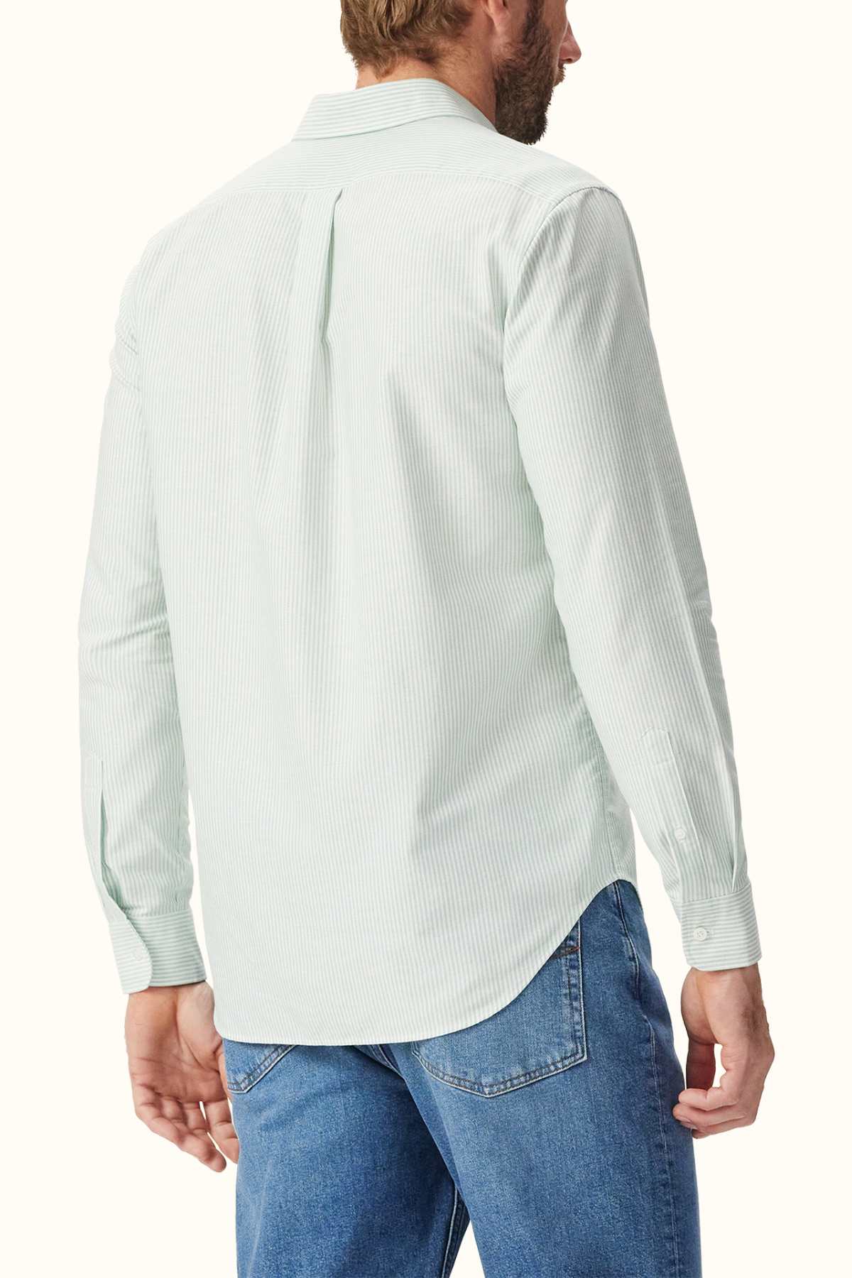 A man is seen from the back wearing an RM Williams Regular Shirt in light green with stripes, crafted from organic cotton. This shirt features long sleeves and a classic collar and is stylishly paired with blue jeans. A pleat at the center back completes the ensemble.