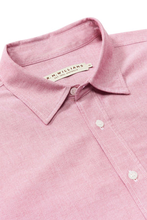 A close-up of the RM Williams Regular Shirt in pink, featuring a slim fit, button-up front, and pointed collar. The label reads "R.M. WILLIAMS Made in Australia." This organic cotton shirt is displayed on a white background.