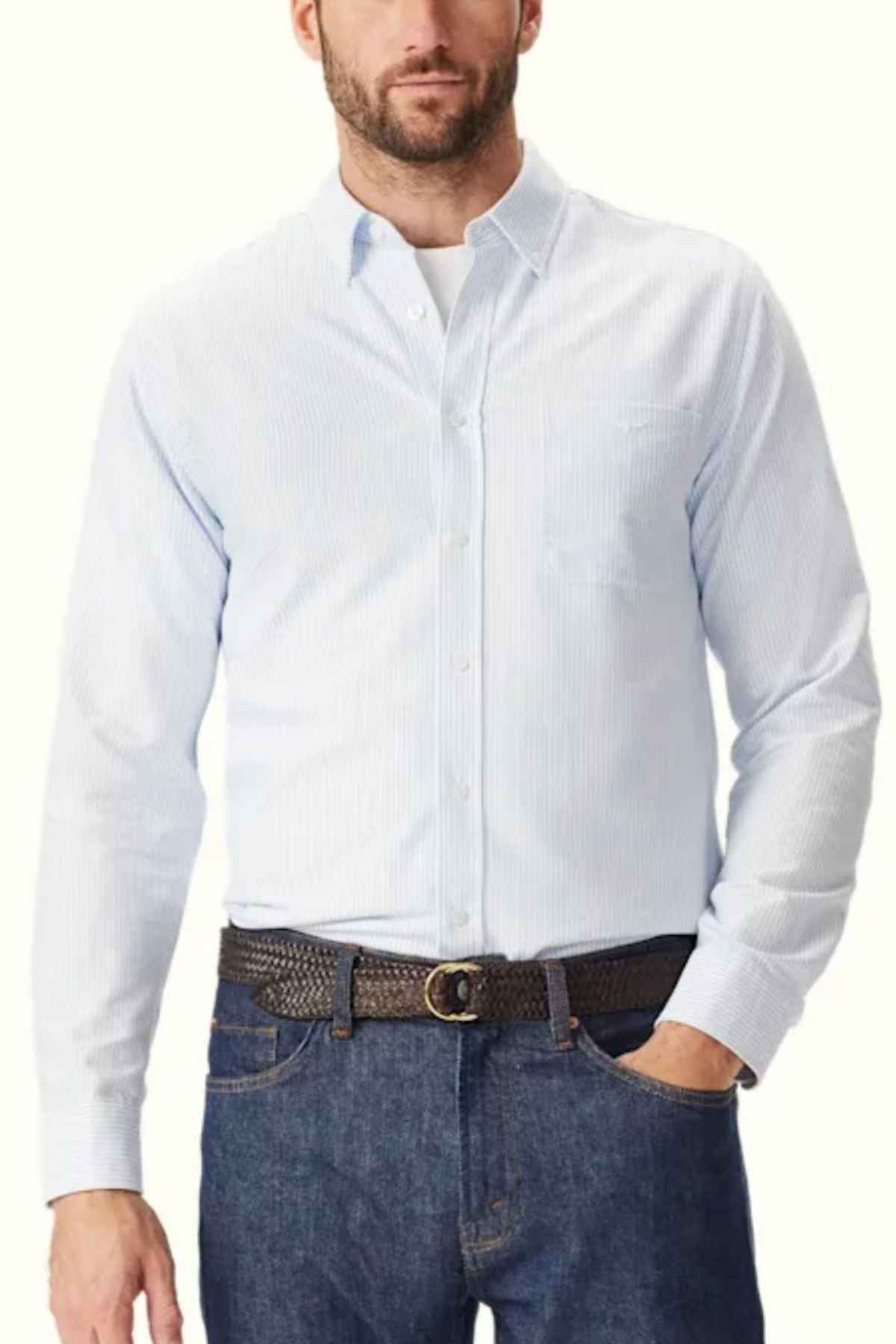 A person is wearing a light blue RM Williams Regular Shirt tucked into blue jeans. They have a brown braided belt with a metal buckle.