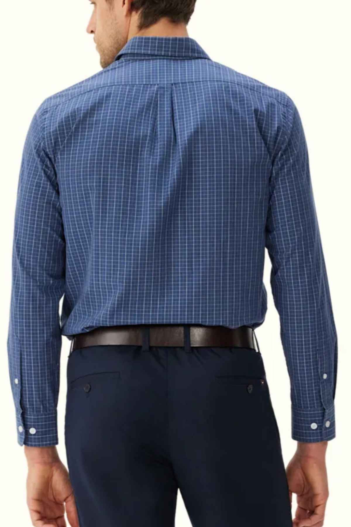 A man wearing an RM Williams Regular Shirt in blue checkered slim fit with a button-down collar, paired with dark dress pants, is seen from the back. He has short, dark hair and is standing against a plain, light-colored background.