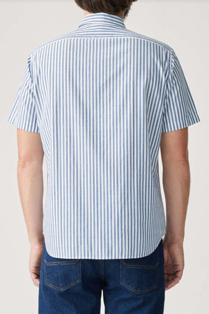 A person is seen from the back wearing the RM Williams Regular Short Sleeve Shirt with blue and white vertical stripes, a button-down collar, and dark blue jeans.