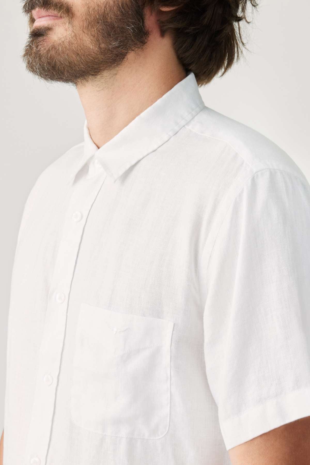 A man wearing the RM Williams Regular Short Sleeve Shirt, made from lightweight oxford cotton in white, is facing slightly to the left. This short-sleeved button-up shirt includes a small chest pocket and is showcased against a neutral background.