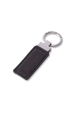 The RM Williams Ridgewood Key Fob is a robust leather accessory with a black rectangular design, stitched edges, and an embossed script logo. It's elegantly attached to a silver metal ring featuring engraved writing for extra sophistication.