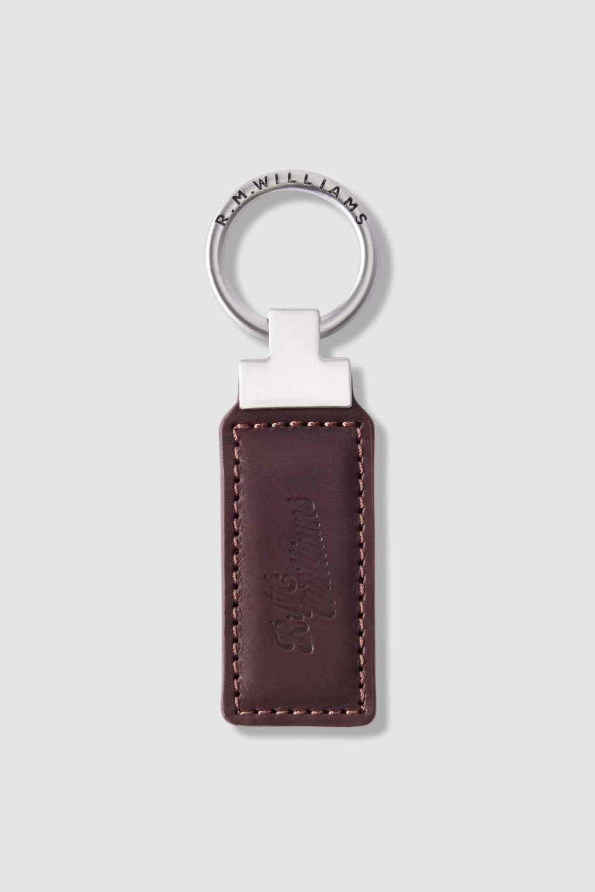 The RM Williams Ridgewood Key Fob features brown Moulton leather with visible stitching and an embossed R.M. Williams logo, attached to a silver ring engraved with "R.M.WILLIAMS," displayed on a light gray background.