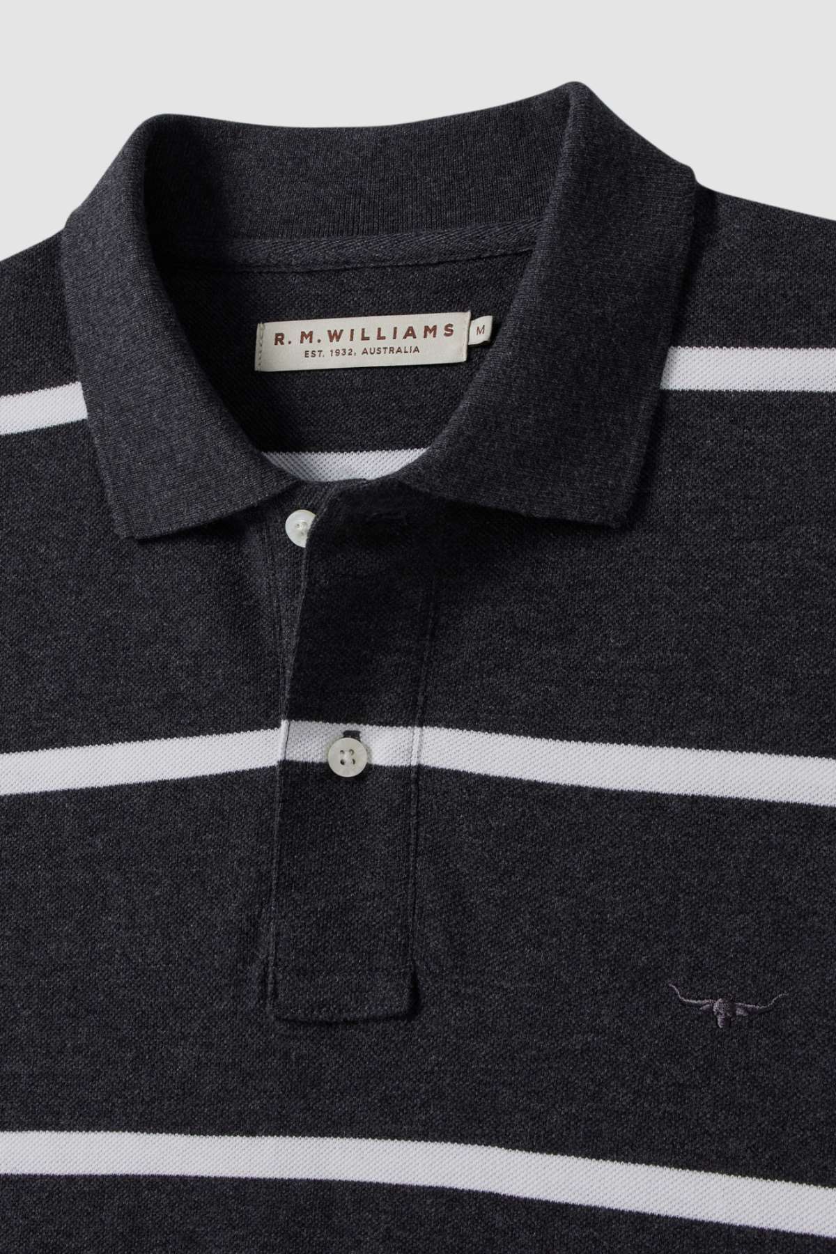 The RM Williams Rod Polo is a black and white striped cotton shirt with a collar, buttons, and small longhorn embroidery on the chest. The label inside the collar reads "R.M. Williams.