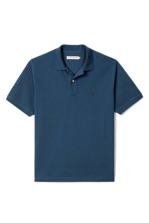 The RM Williams Rod Polo is a dark blue, short-sleeve collared shirt with a button placket and a small embroidered logo on the left chest, displayed flat on a white background.