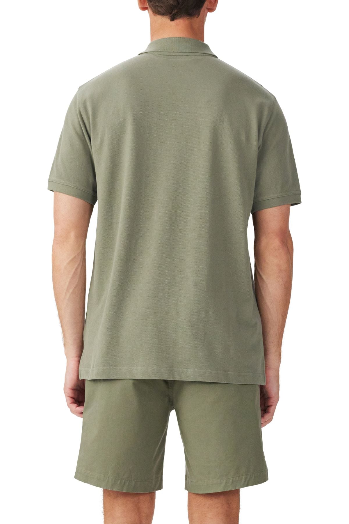 A man stands with his back to the camera in a matching olive green RM Williams Rod Polo organic cotton pique short-sleeve shirt and shorts set, set against a plain white background.
