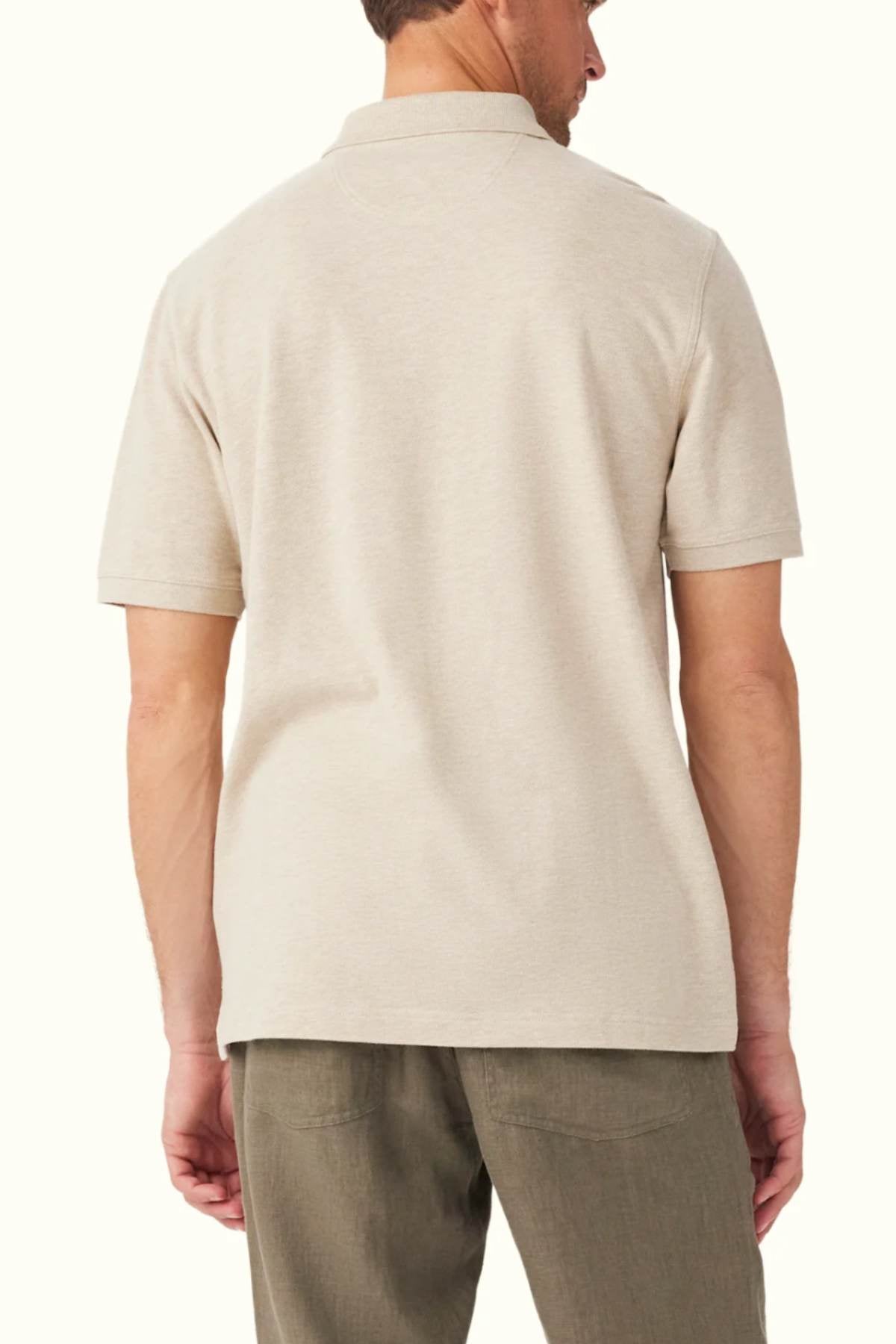 A man wearing the RM Williams Rod Polo, a beige, classic-fit, short-sleeve shirt made from breathable cotton pique, and olive green pants stands with his back to the camera against a plain off-white background.
