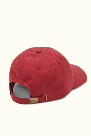 The RM Williams Script Cap, in red cotton twill, features an adjustable strap and a metal buckle engraved with a small R.M.Williams logo for sophistication against a light background.