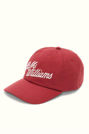 The RM Williams Script Cap is crafted from cotton twill and features white embroidered script on the front. This cap includes eyelets for ventilation and has a slightly curved brim, showcased against a light background.