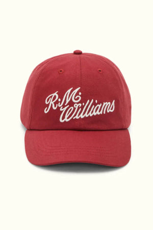 The RM Williams Script Cap is made of cotton twill, features "R.M. Williams" in white script on the front, and has a curved brim with a minimalist red design.