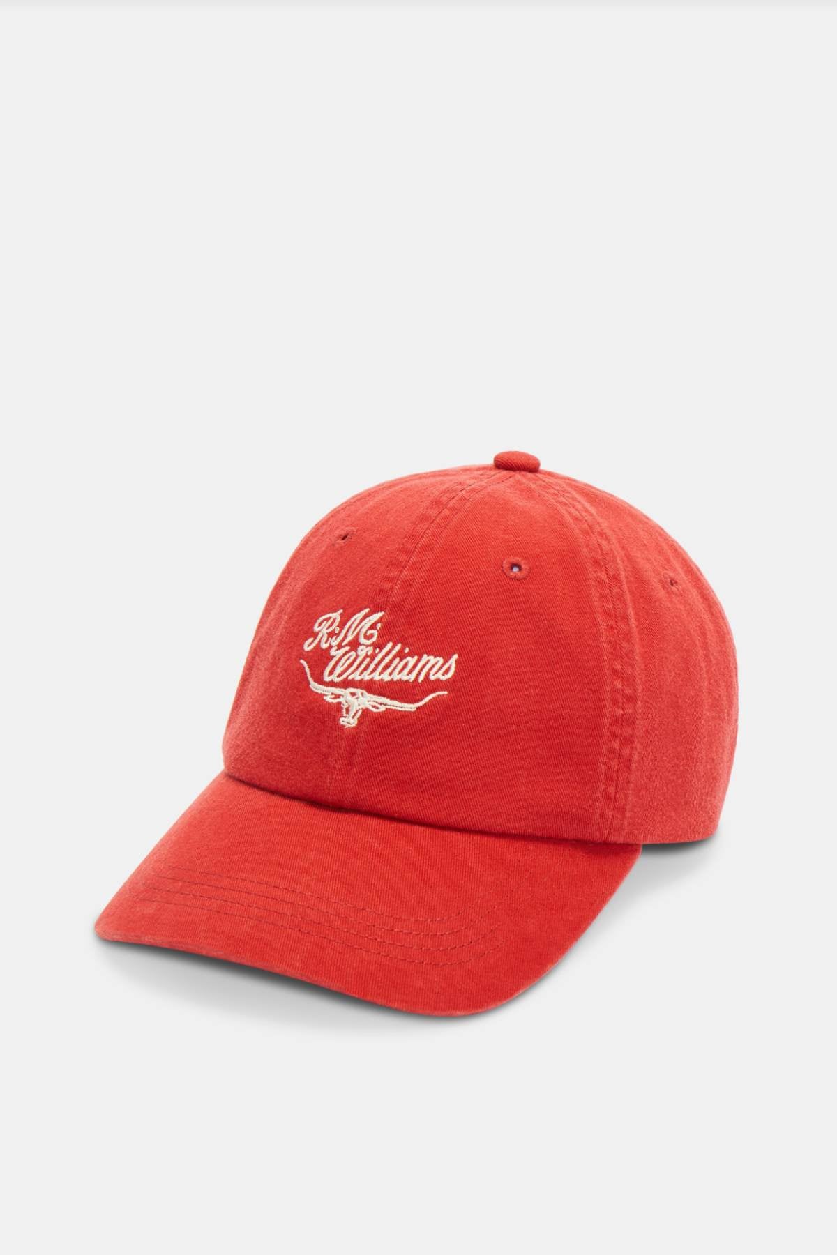 The RM Williams Script Longhorn Cap is a vibrant red baseball cap made from washed cotton twill. It features white embroidered text and a heritage script logo on the front, complemented by a curved brim and an adjustable strap at the back. The neutral background accentuates its vivid color and timeless design.