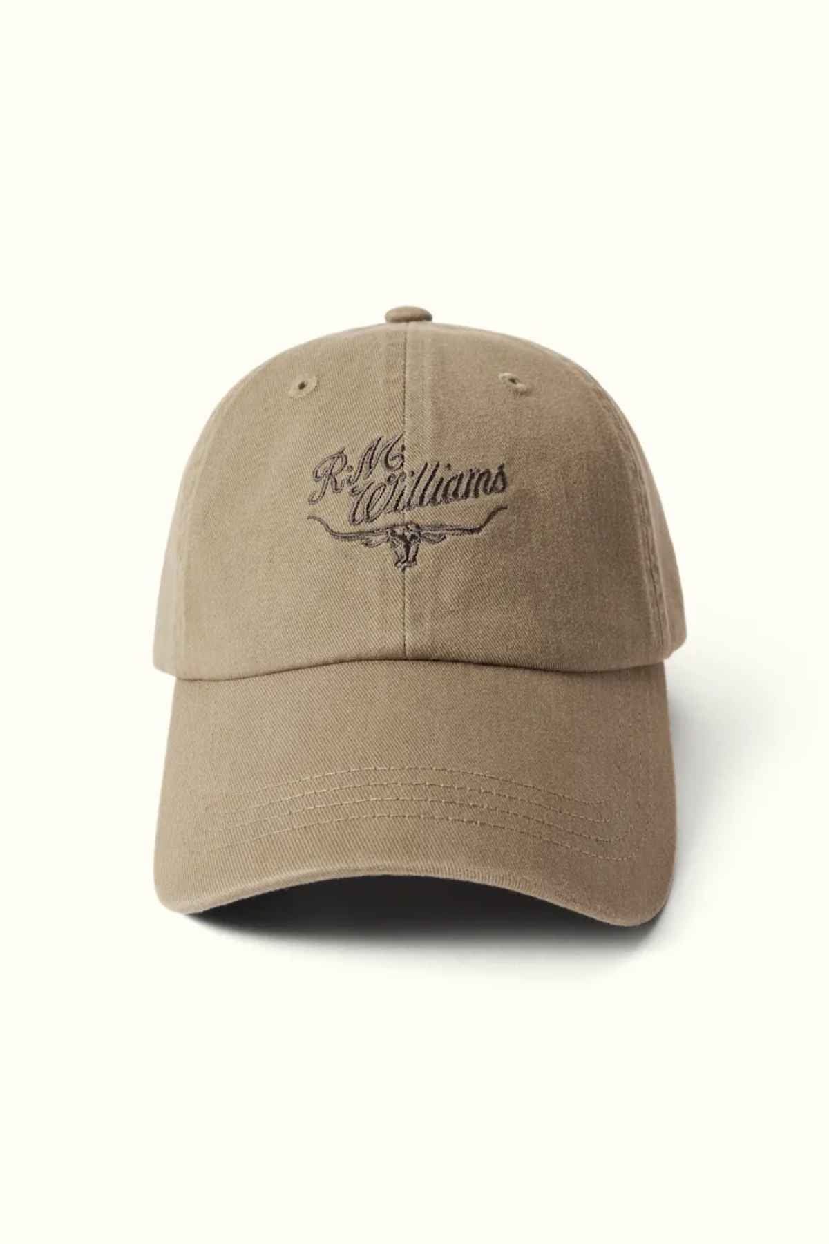 The RM Williams Script Longhorn Cap is a brown baseball cap made from washed cotton twill, featuring "R.M. Williams" embroidered in dark brown on the front above an illustration of longhorn cattle horns.