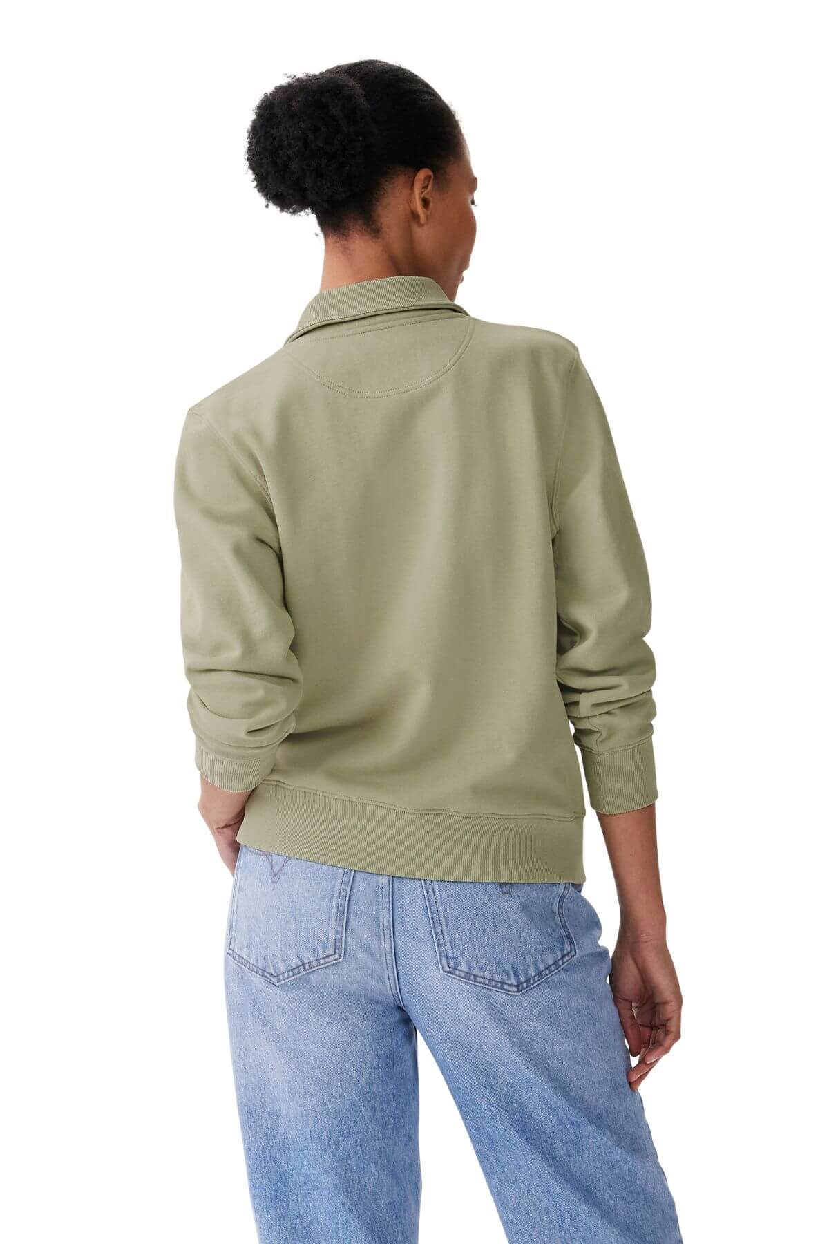 A person with dark, curly hair in a bun is seen from behind wearing an RM Williams Trickett Zip Neck Sweatshirt in light green and blue jeans, standing against a plain white background.