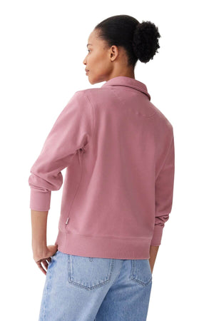 A person with short hair styled in a bun is seen from the back wearing an RM Williams Trickett Zip Neck Sweatshirt, adorned with longhorn embroidery and light blue jeans, standing against a plain white background.