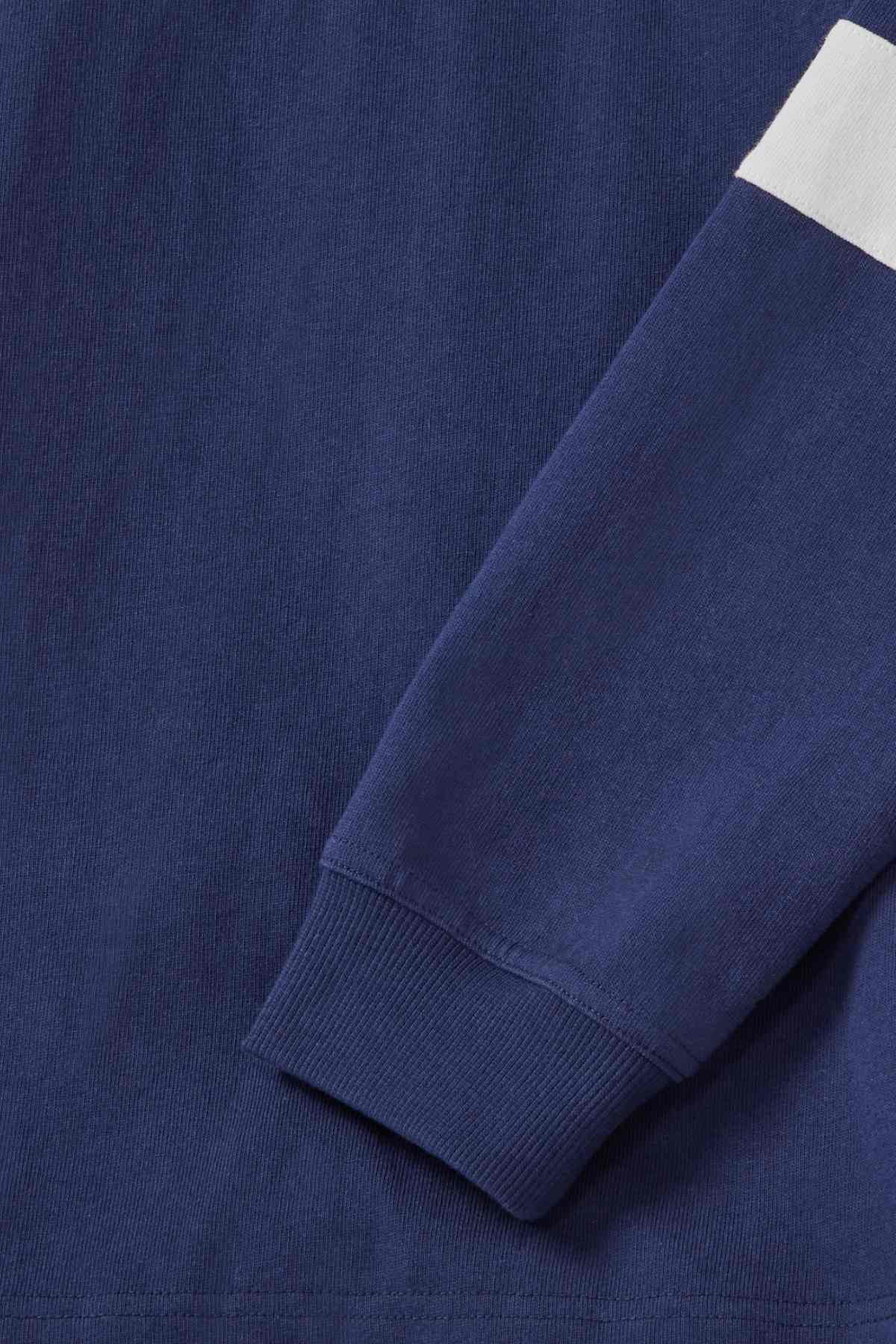 Close-up of the RM Williams Tweedale Rugby shirt in navy blue, showcasing its ribbed cuff at the wrist and a horizontal white stripe on the upper arm. The material looks comfortable with a slight texture, likely indicating cotton or a blend, and is adorned with subtle longhorn embroidery for an added touch of detail.