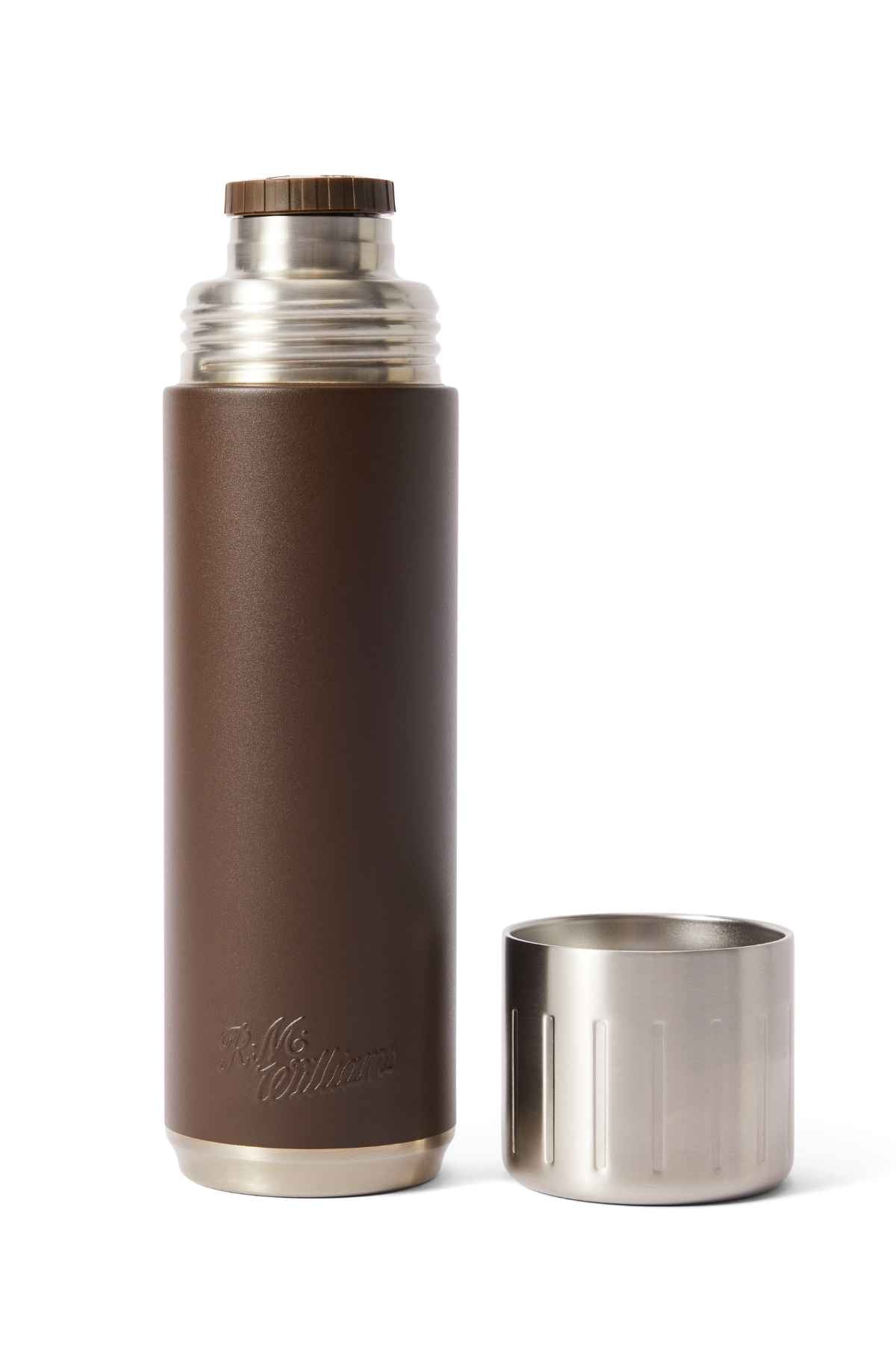 The RM Williams Vacuum Flask is brown with a silver metallic top and cap. The cap sits beside the flask, which features stainless steel double-wall vacuum insulation and an engraved brand name.