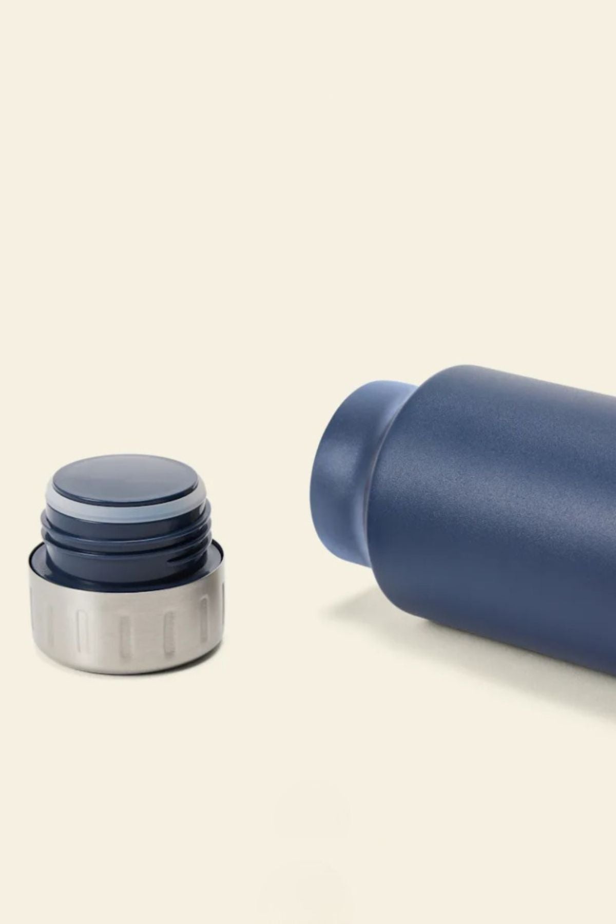 A close-up of the RM Williams Water Bottle, a blue stainless-steel vacuum flask with its cap removed, lying on its side against a beige background—ideal for keeping drinks at the perfect temperature on any adventure.