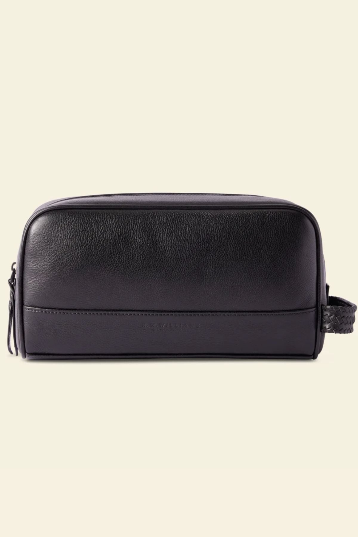 The RM Williams Farrier Signature Washbag is a black tumbled grain leather toiletry bag with a rectangular design, zip closure, water-resistant lining, and woven side handle, shown on a plain cream background.