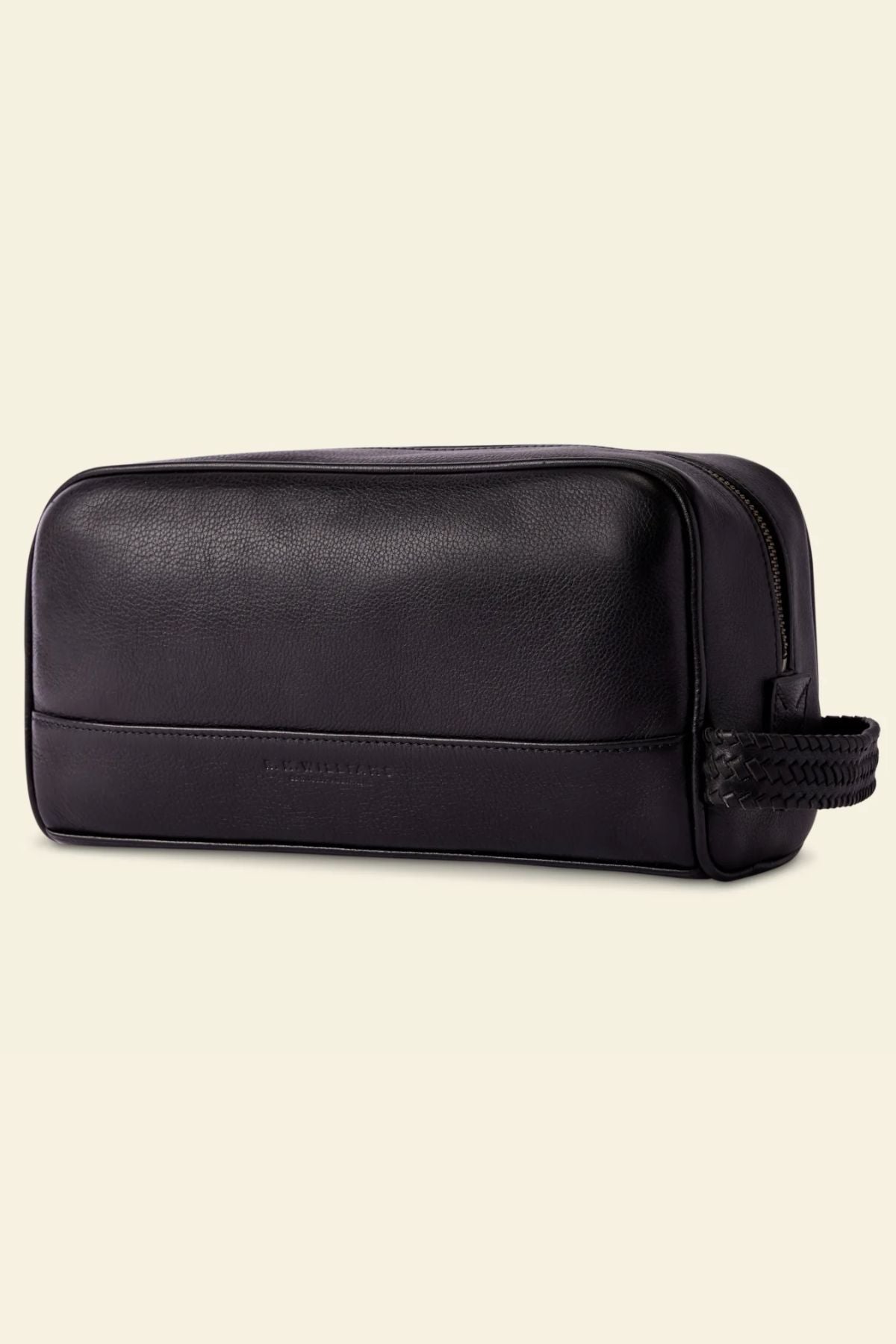 The RM Williams Farrier Signature Washbag is a black tumbled grain leather toiletry bag with a rectangular shape, zippered top, and braided end handle, shown against a plain light background.