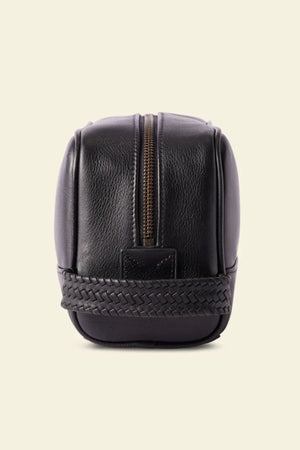 The RM Williams Farrier Signature Washbag, crafted from black tumbled grain leather with a woven base detail, is shown upright against a light background—perfect for use as a travel toiletry bag.