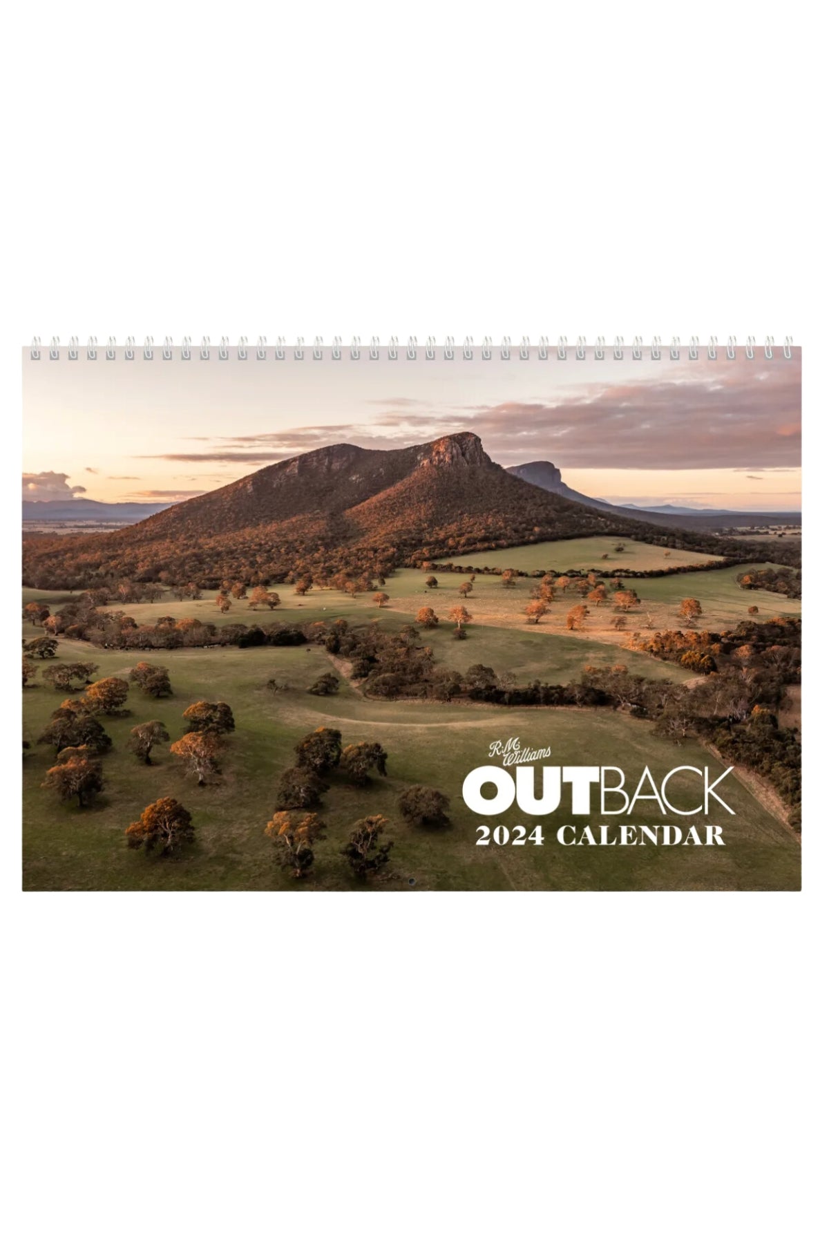 The RM Williams Outback Calendar 2024 features stunning photos by leading Australian rural and regional photographers, with a cover showcasing an aerial view of rugged mountains at sunset, rolling fields, and scattered trees.
