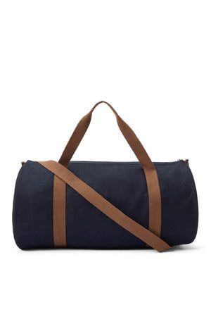 The RM Williams Heritage Bag is a cylindrical navy blue cotton canvas bag with brown shoulder and hand straps, plus an adjustable crossbody strap for versatile carrying. Shown against a white background.