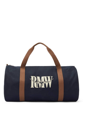 The RM Williams Heritage Bag is a navy blue cotton canvas bag with brown handles, a zipper, and bold white "RMWW" heritage logo on the front.