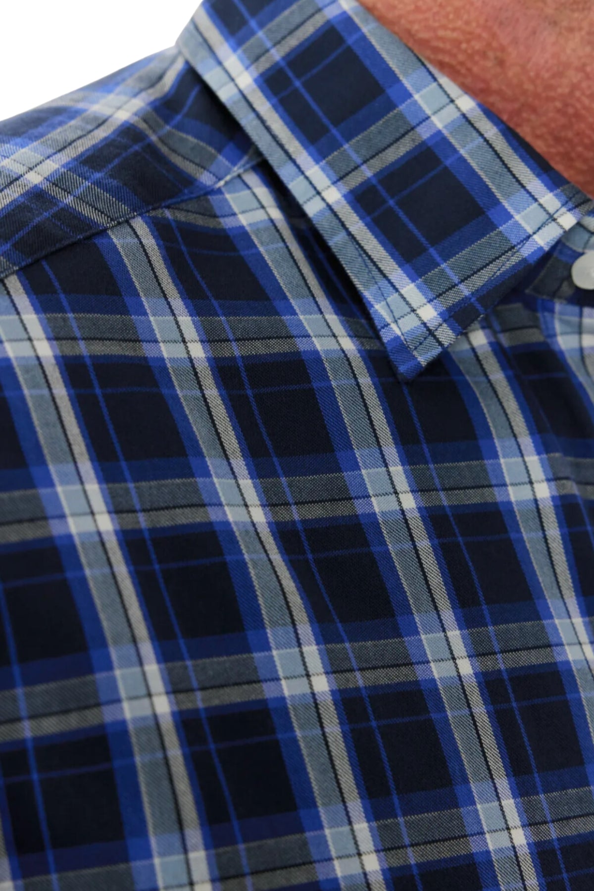 Close-up of a person wearing the RM Williams Hervey Shirt. The shirt features a blue, black, and white plaid design with a classic tartan pattern, showcasing intersecting lines in various shades of blue and white. The partially visible collar and short-sleeve silhouette enhance the comfort provided by its breathable cotton material.