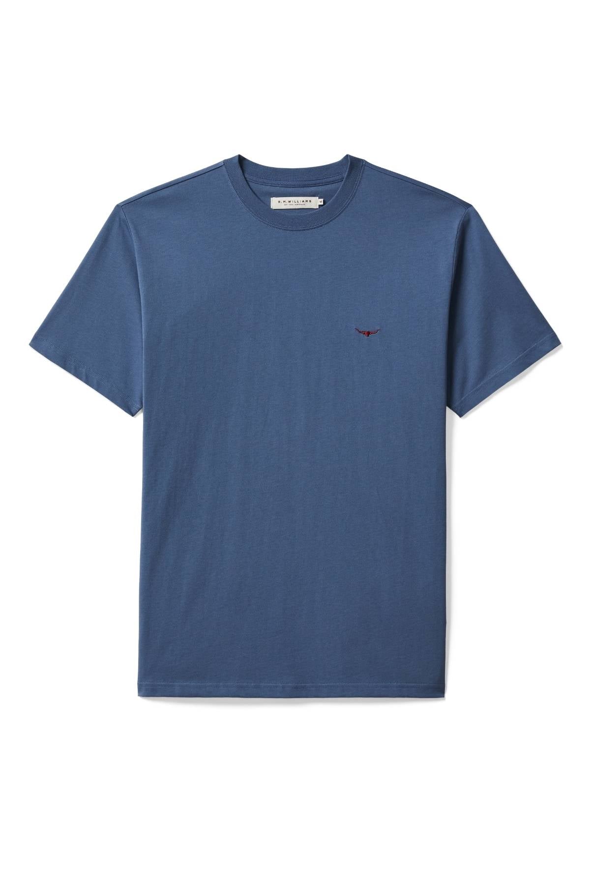 The RM Williams Parson T-Shirt is a plain blue short-sleeve tee with a ribbed crew neck and a small red Longhorn logo embroidered on the left chest, laid flat on a white background.