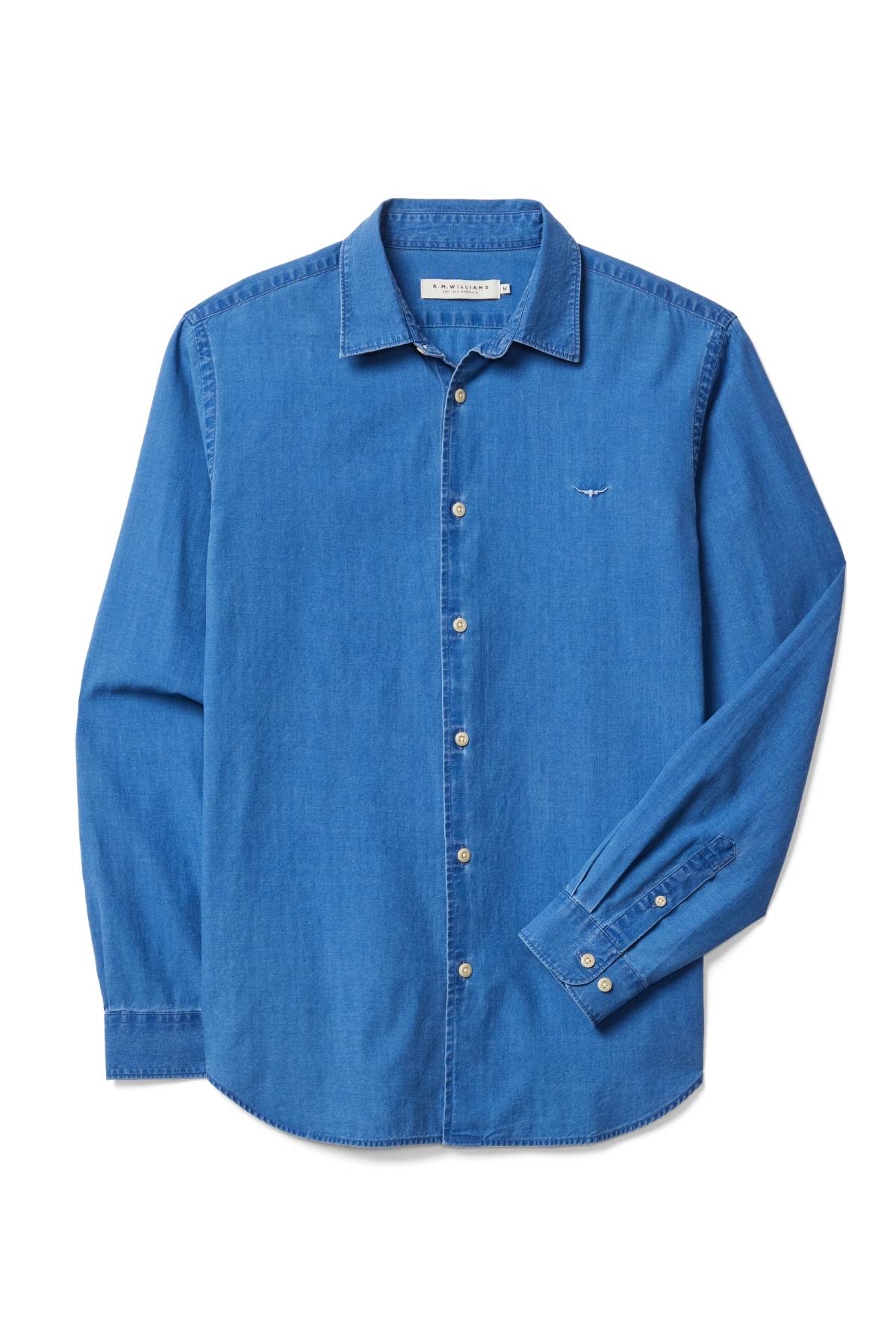 The RM Williams Arno Regular Indigo Shirt is a long-sleeve, button-down denim shirt in medium blue with a classic collar, French placket, branded buttons, and a subtle Longhorn embroidery on the left chest.