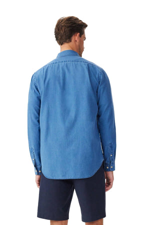 A man faces away from the camera, wearing the RM Williams Arno Regular Indigo Shirt and dark navy shorts, set against a plain white background.