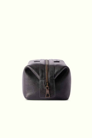 The RM Williams Farrier Washbag, crafted from black leather with a frog-mouth zipper, is displayed against a light background. It stands upright with its zipper slightly open, highlighting its textured surface and structured design.