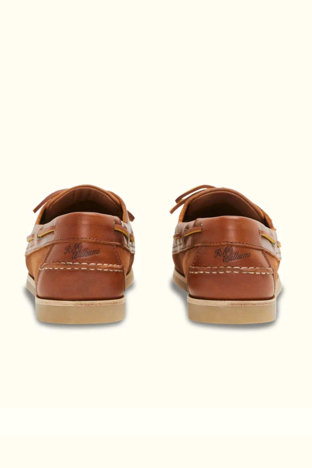 Two RM Williams Hobart Boat Shoes in brown bovine leather, viewed from the back, showcase beige soles and stitching. The brand name is visible on each heel, making them perfect for casual wear.