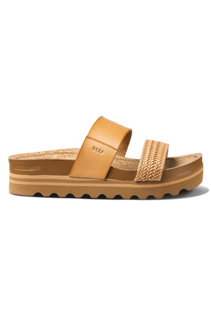 The REEF Cushion Vista Hi TX is a tan platform sandal with a wide leather strap, woven detail, cushioned midsole, cork footbed, and ridged rubber sole—stylish and sustainable for everyday wear. "Reef" logo featured on strap and footbed.