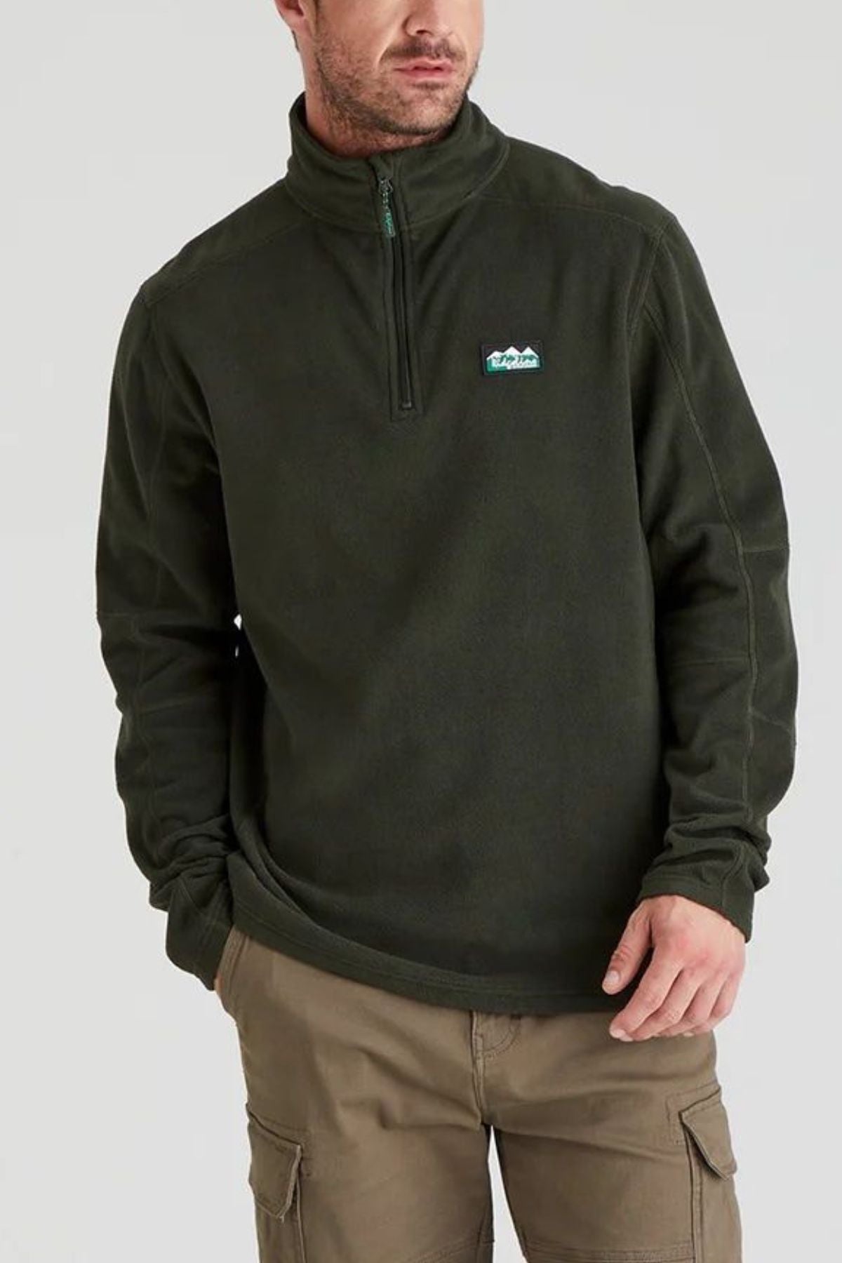 A man wears the Ridgeline Narvik Fleece, a dark green quarter-zip pullover with quick-drying fabric and a mountain logo, paired with tan cargo pants. He stands with one hand in his pocket against a plain background.