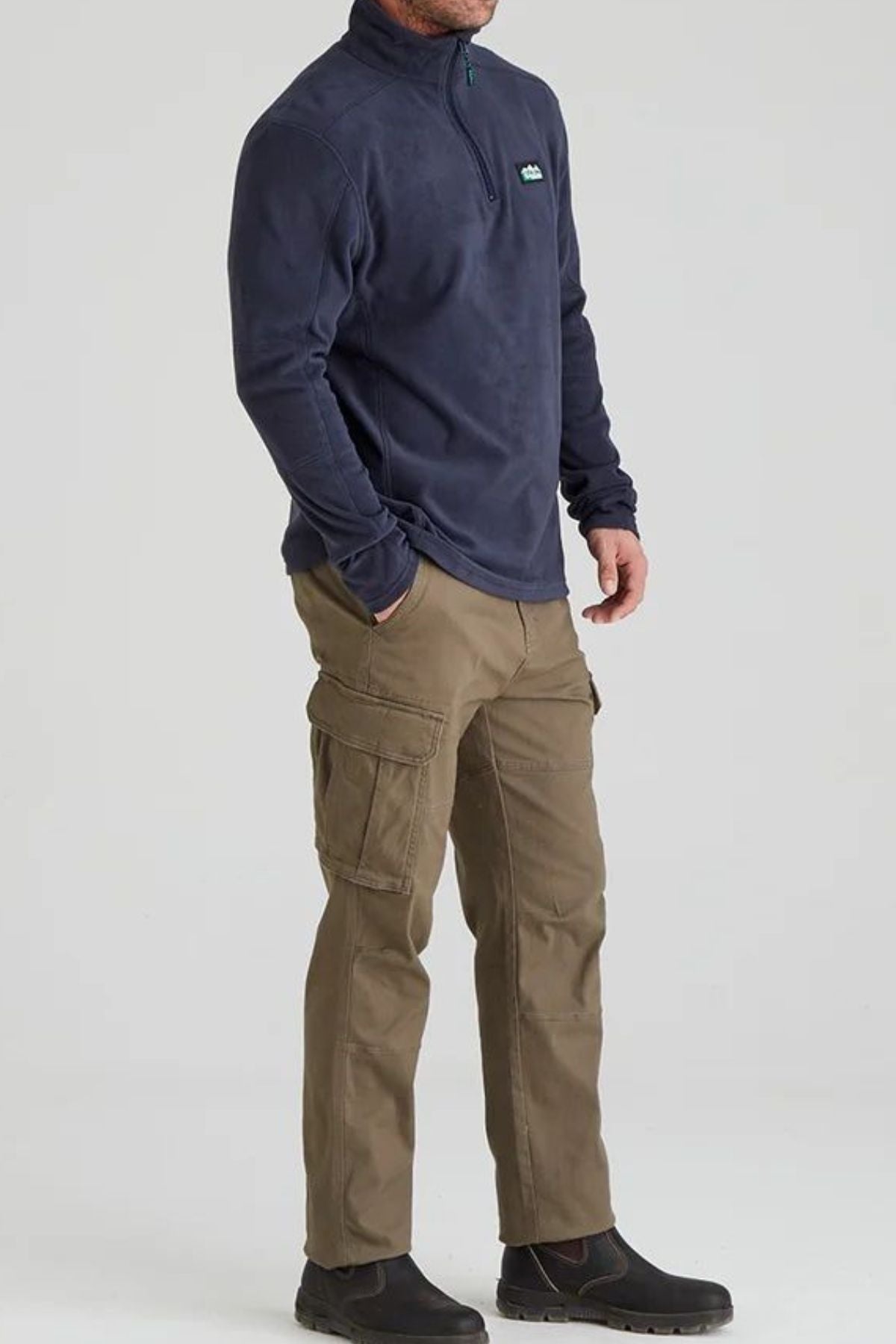 A person wearing the Ridgeline Narvik Fleece in navy, khaki cargo pants, and black boots stands against a plain light background.