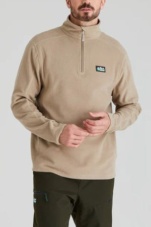 A man wearing a Ridgeline Narvik Fleece lightweight zip-neck pullover with a small chest logo and dark green pants stands against a plain light background.