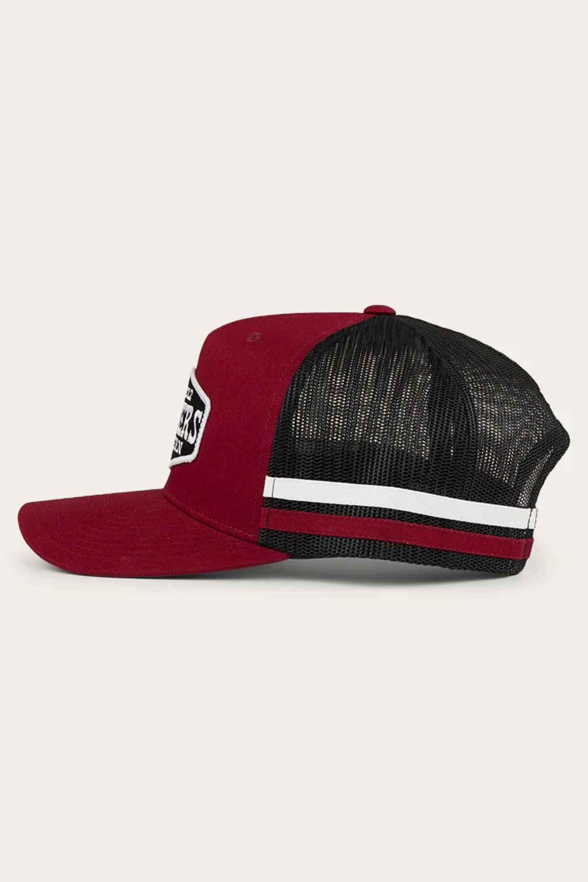 Side view of the Ringers Western Banks Trucker Cap in red and black, featuring a curved brim and mesh back. The front showcases a white patch with text, complemented by a white stripe running across the mesh section. Crafted from durable cotton twill, this stylish cap includes a convenient snapback closure, all set against a plain background.