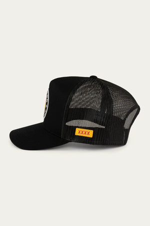 The Ringers Western Can Trucker is a black cap with a twill front and poly mesh back, featuring a round patch with black, yellow, and white embroidery on the front panel, and a yellow rectangular patch with red "XXXX" text on the side against a light gray background.