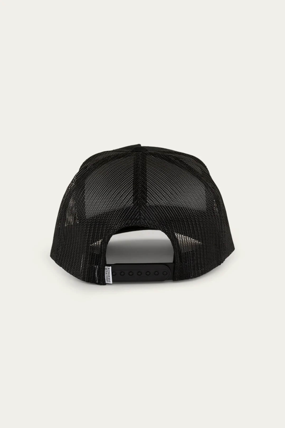 Rear view of a Ringers Western Can Trucker cap featuring a black mesh back and adjustable snapback; poly mesh enhances ventilation for a light feel. Background: light cream.