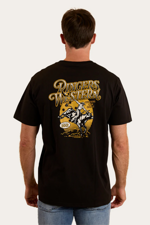 A man wears the Ringers Western Cowboys Can Dance Loose Fit T-Shirt, featuring a yellow and white "Cowboys Can Dance" graphic, a cowboy riding a bull, stars, and the year 2012 on the back.